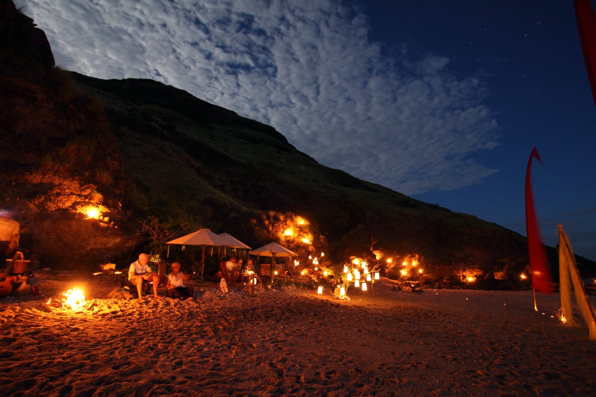 Lantern-lit private beach dinner under stars with Silolona anchored offshore