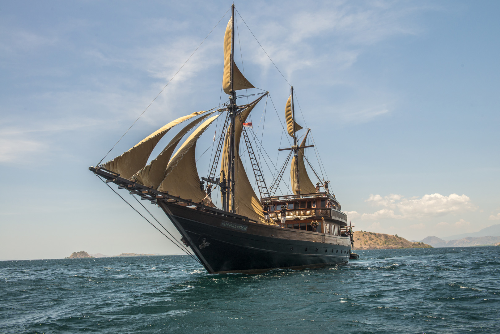Bow view of Alila Purnama phinisi under sail with crew on deck