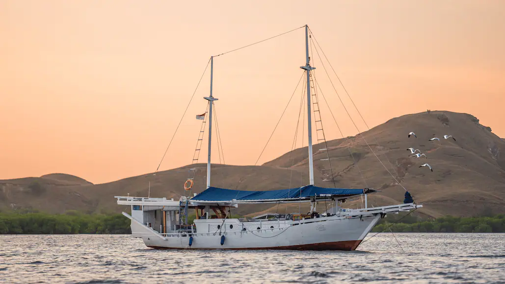 Jinggo Janggo phinisi anchored at sunset with hills behind in Komodo