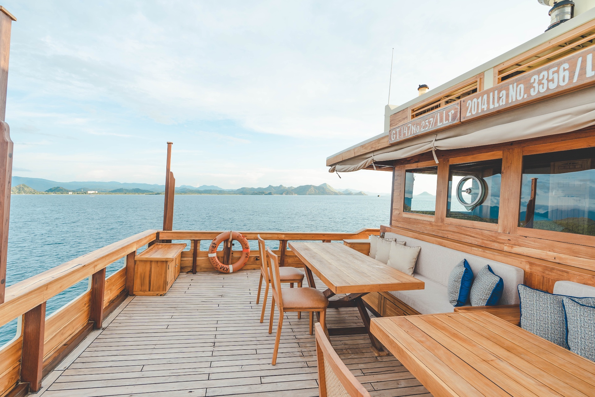 Mischief aft deck dining area with wooden table, cane chairs and cushioned bench alongside the wheelhouse