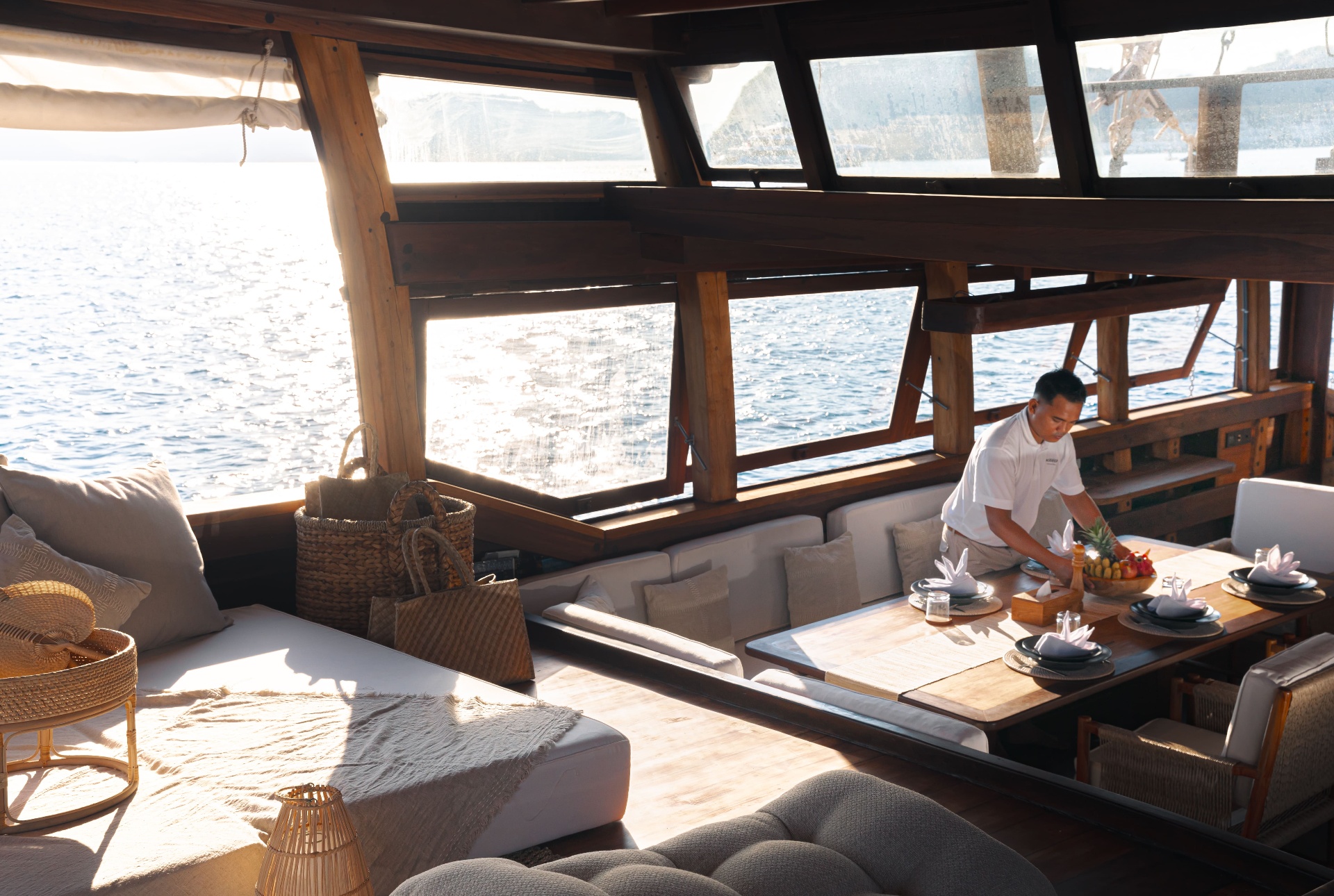 Crew setting Nataraja's main-deck table with the sea reflecting through the windows behind