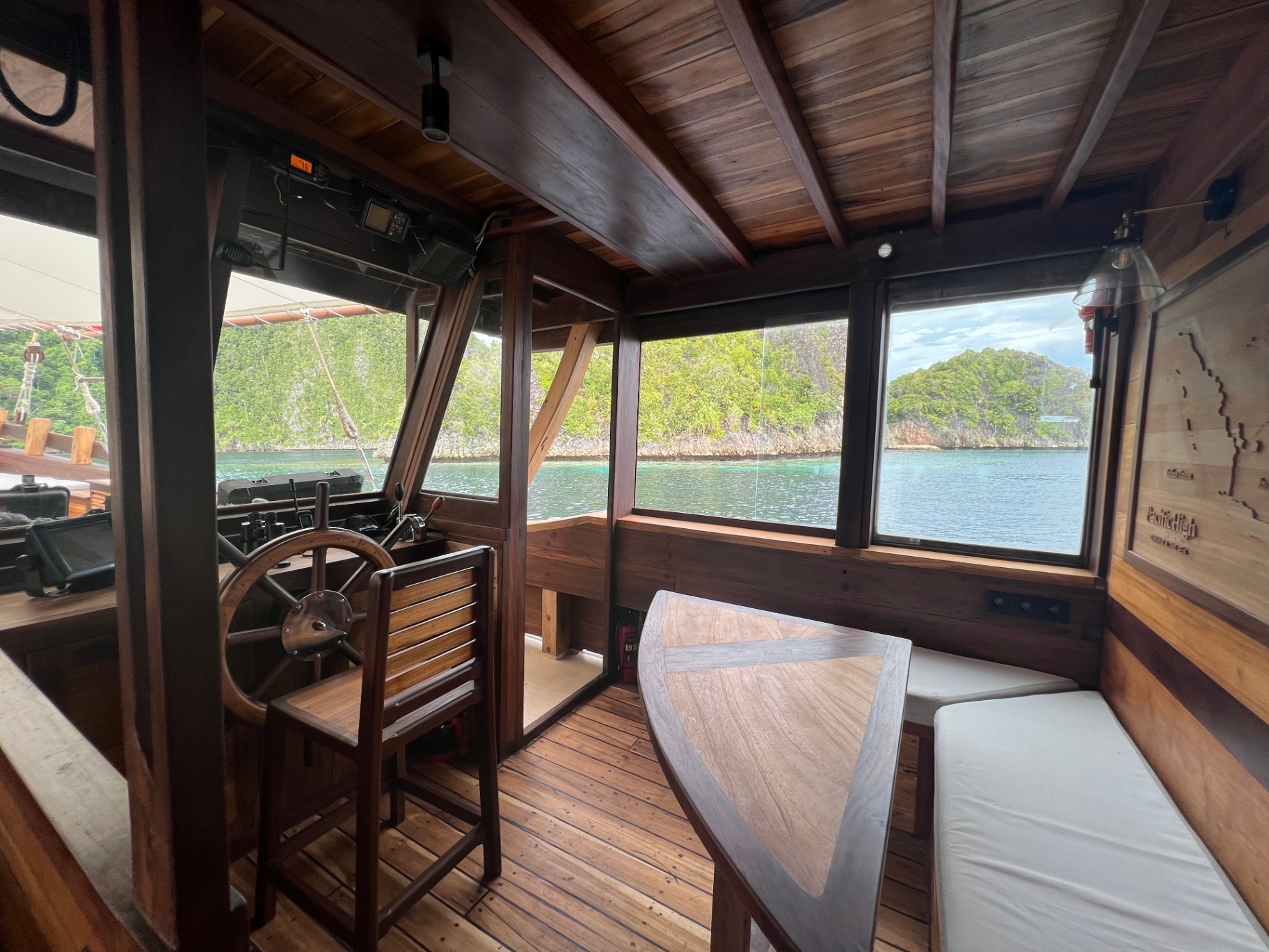 Dewata wheelhouse with wooden helm and windows over turquoise Raja Ampat water
