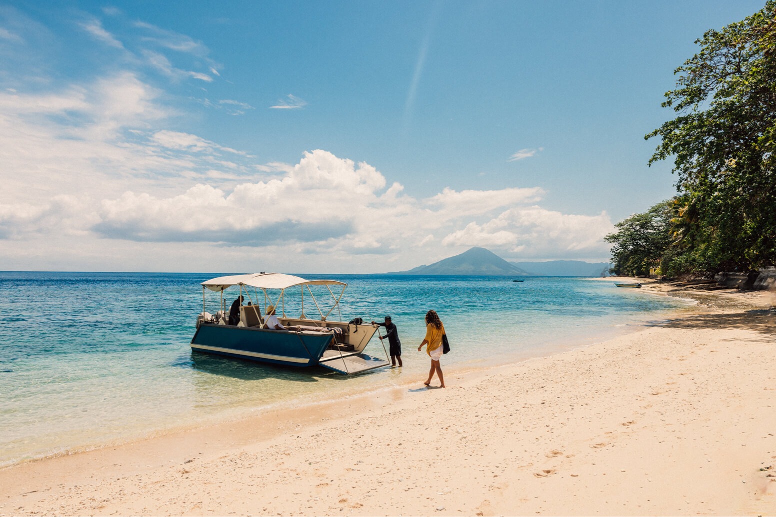 Tender landing on a white-sand beach with a distant volcano