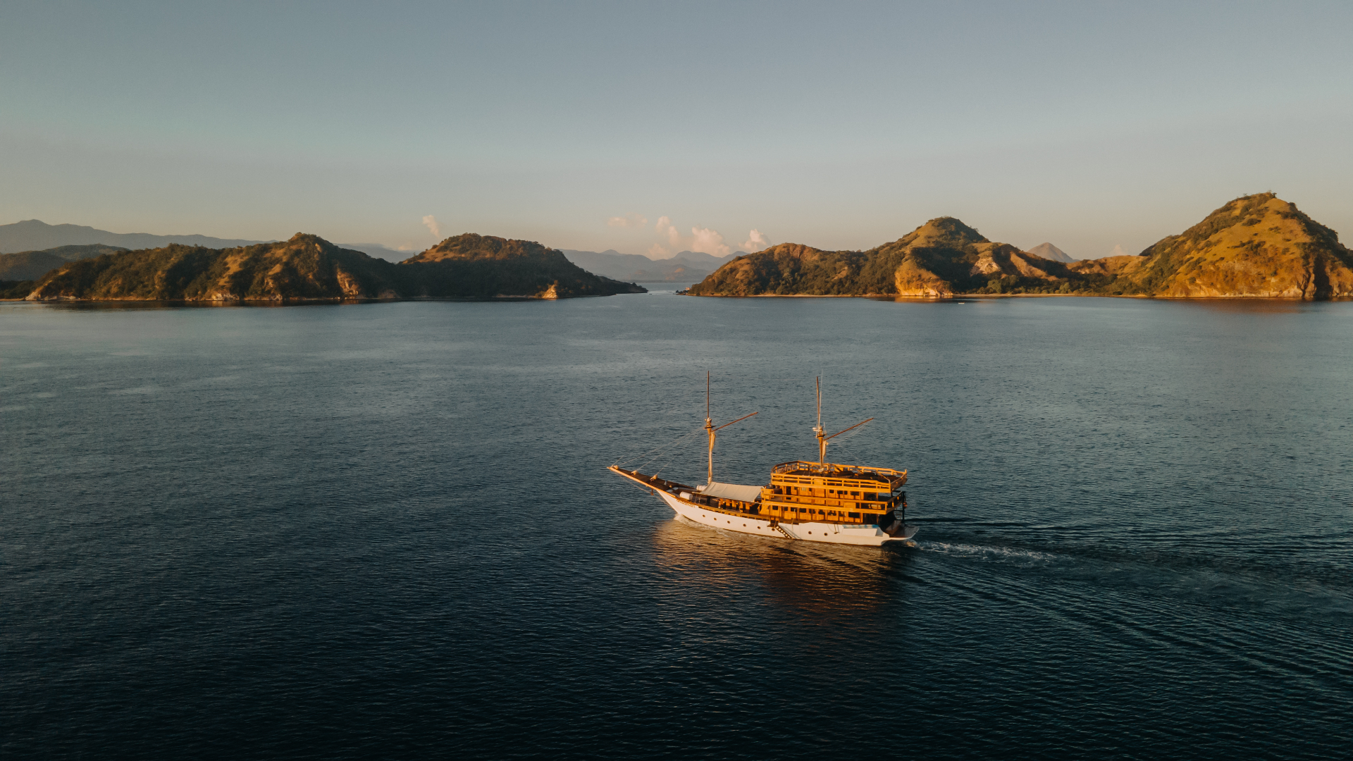 Andamari cruising in warm evening light with green islands lit by the setting sun behind