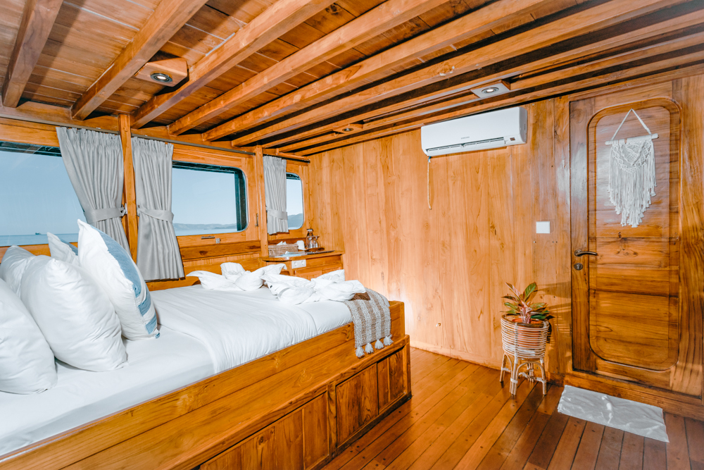 Master cabin on Adishree with white linens, teak walls, air-conditioning and a window looking over the sea