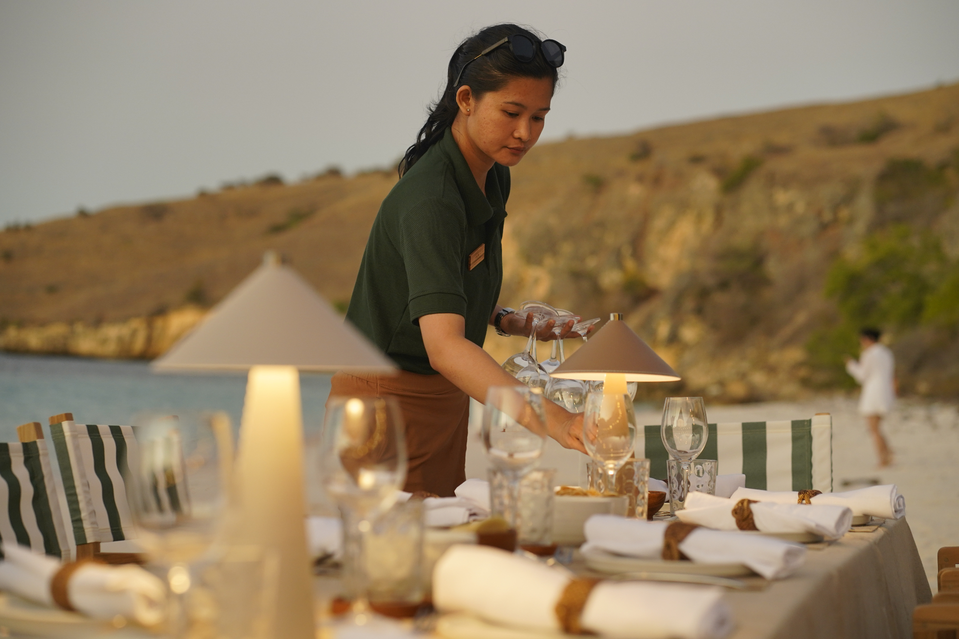 Sanctuary crew member setting wine glasses on a beach dinner table at sunset