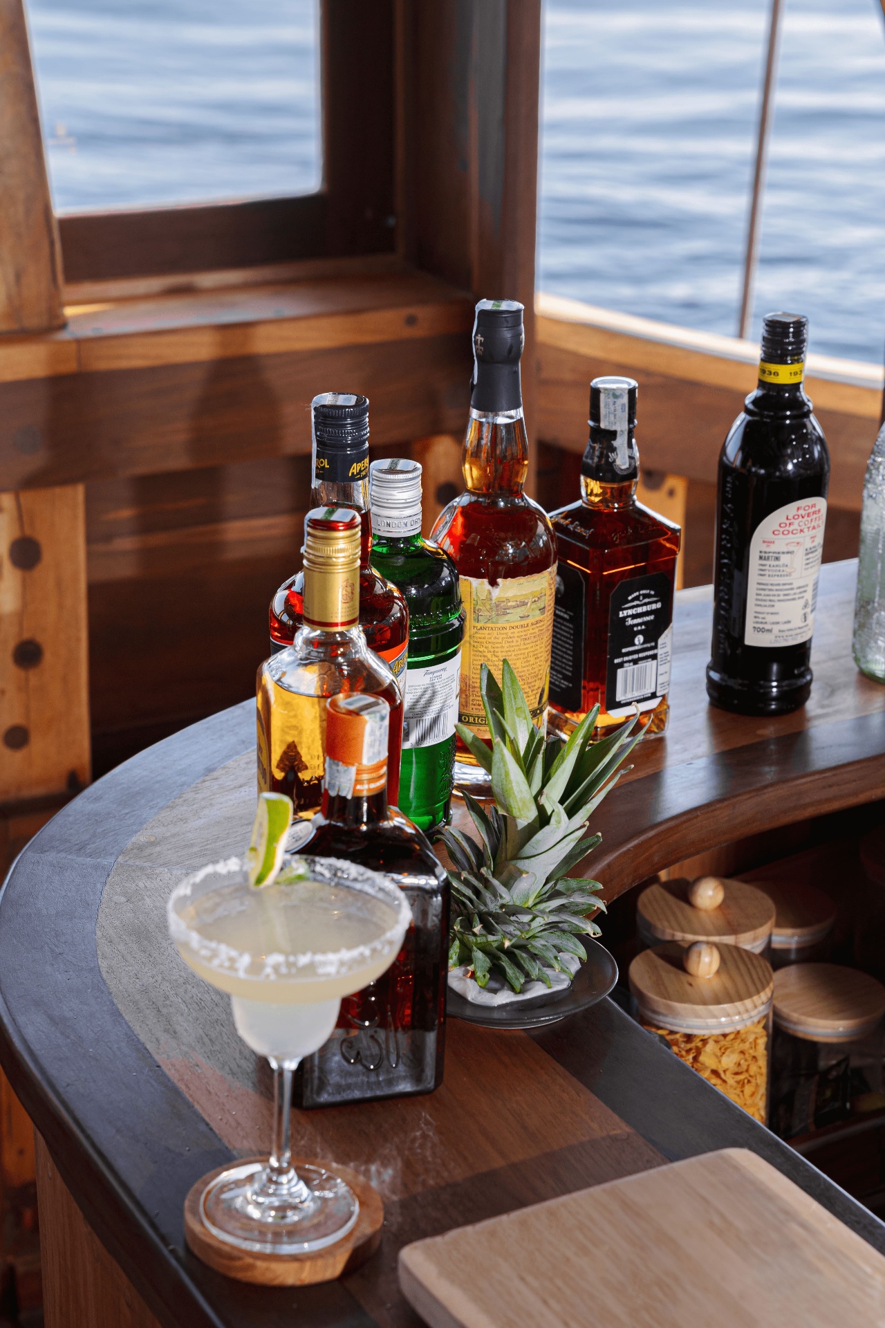 Cocktail on Nataraja's teak bar with premium spirits lined up and open sea through the window
