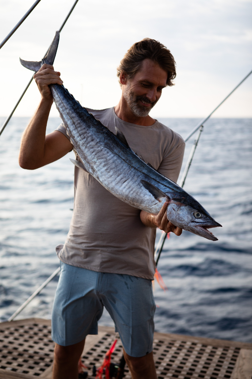 Guest holding a freshly caught wahoo on the aft deck at sunset