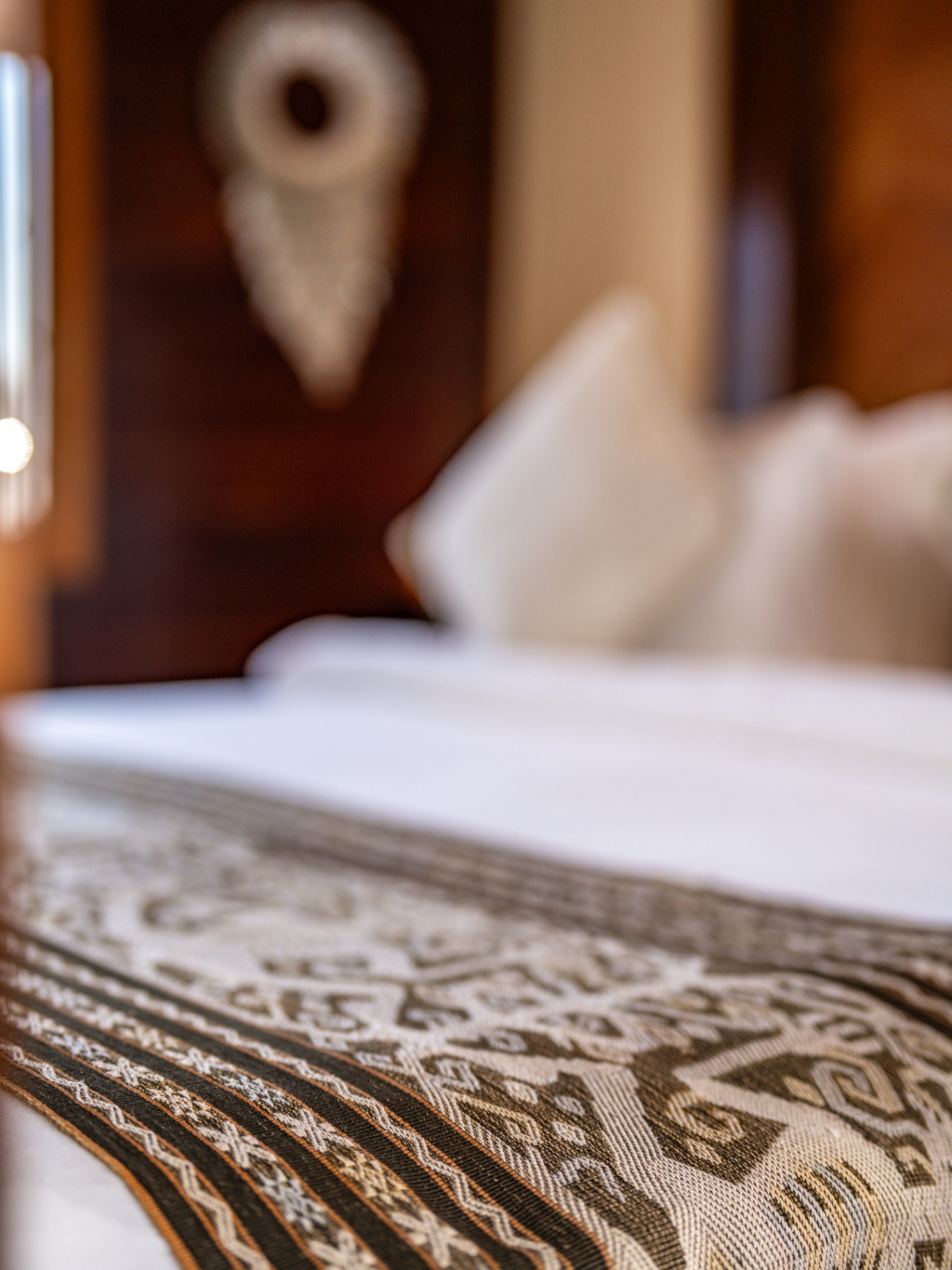Close-up of a handwoven ikat bed runner on a Lamima suite bed with carved teak headboard behind