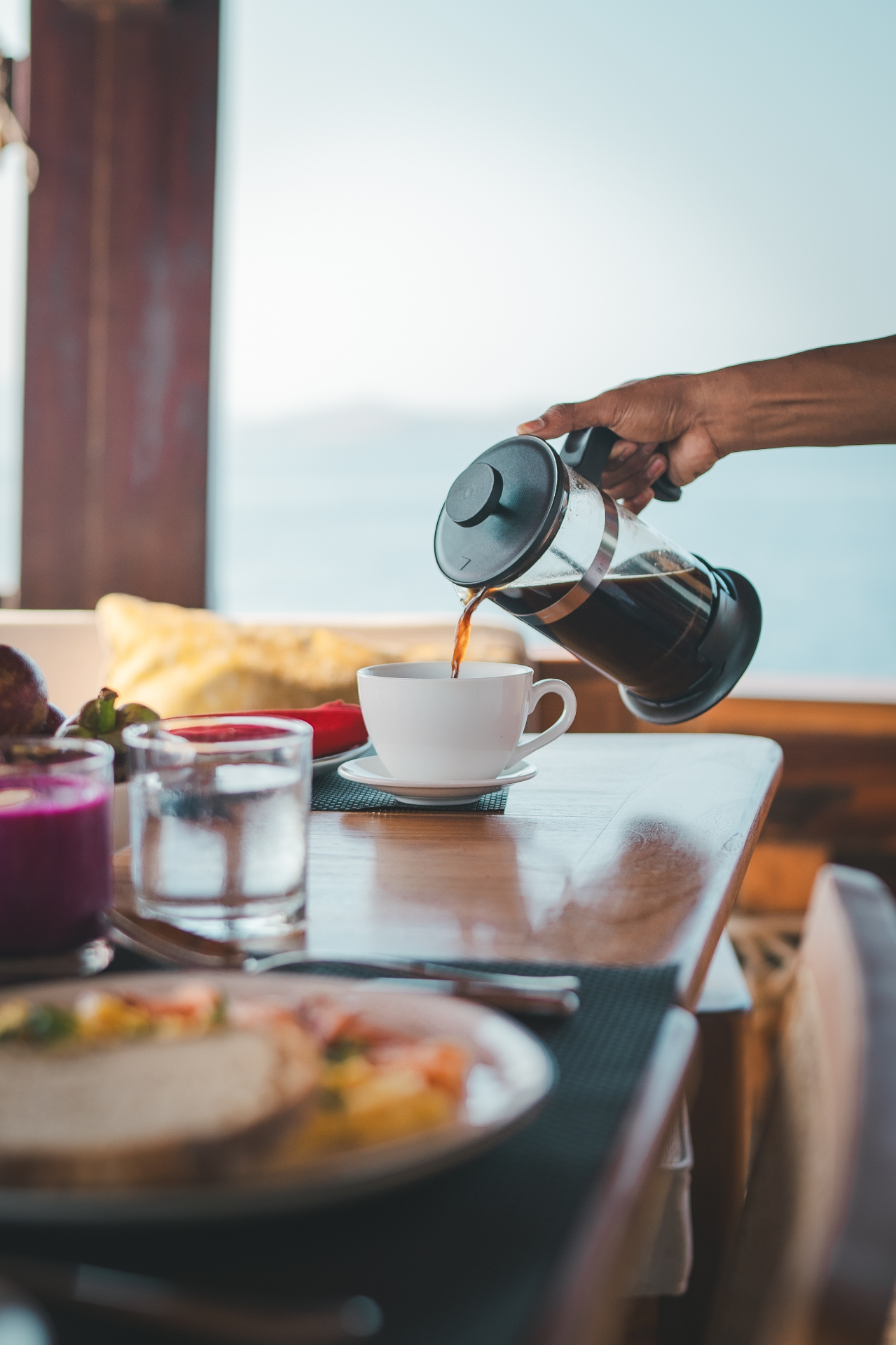 French press coffee being poured into a white cup on Mischief's dining table with sea view
