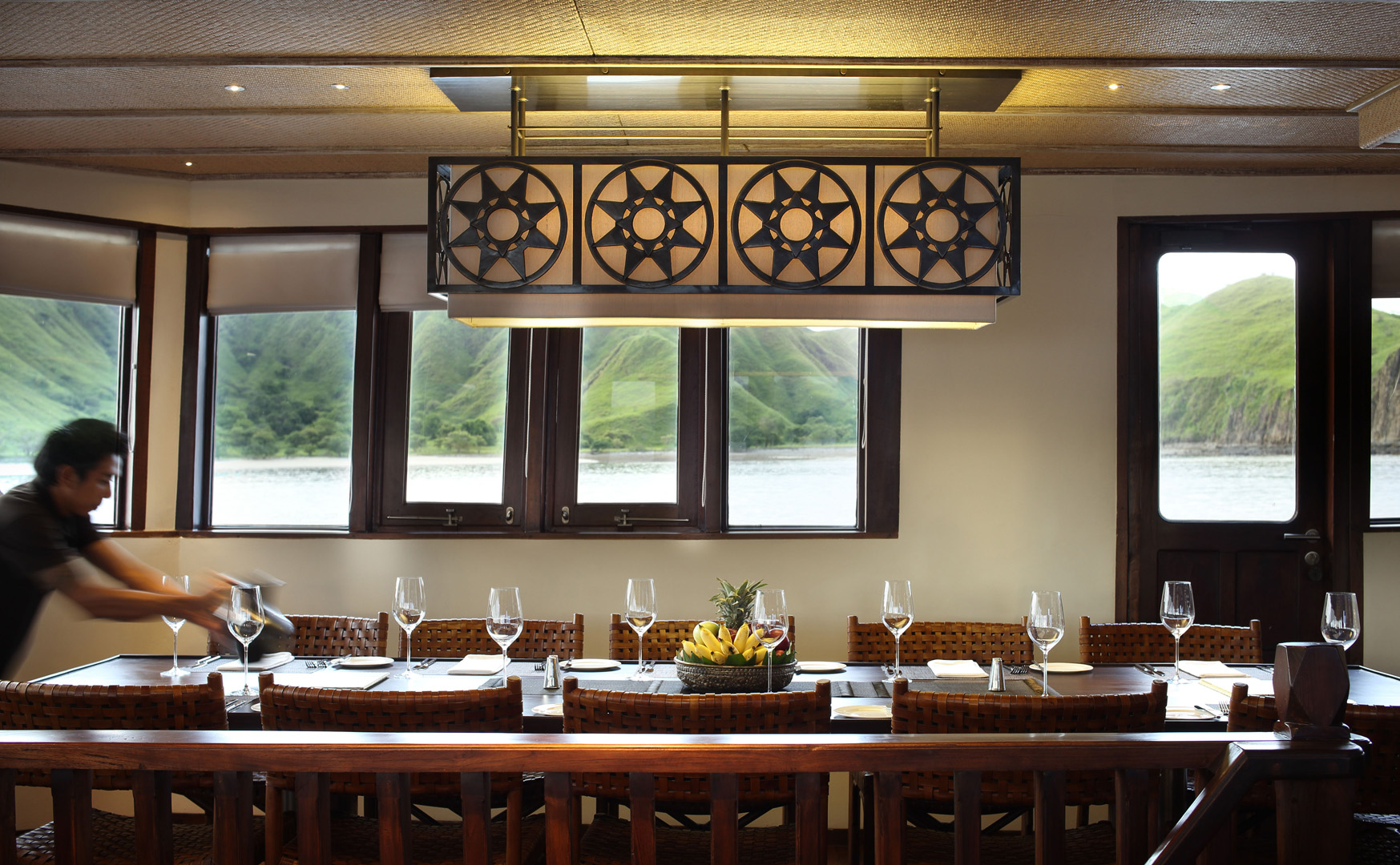 Indoor dining table on Alila Purnama set for dinner with woven leather chairs and pendant lamp